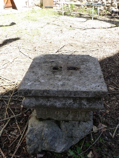 Socle de croix déposé dans le jardin.