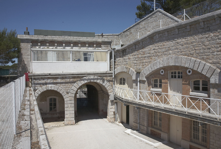 Porche sur cour de l'entrée et bâtiment (b) sur la porte, extrémité ouest de la façade de la caserne.