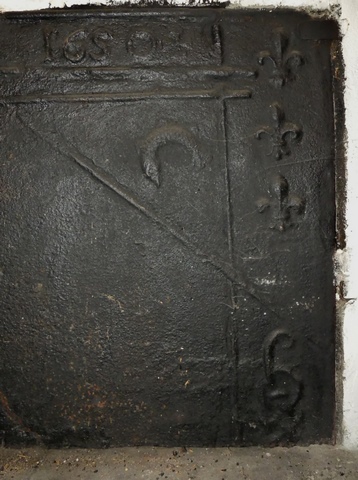 Partie nord. Rez-de-chaussée surélevé, cuisine. Mur sud, cheminée. Plaque foyère en fonte moulée : date portée (1650), fleur de lys, dauphin et initiales entrelacées. Détail.