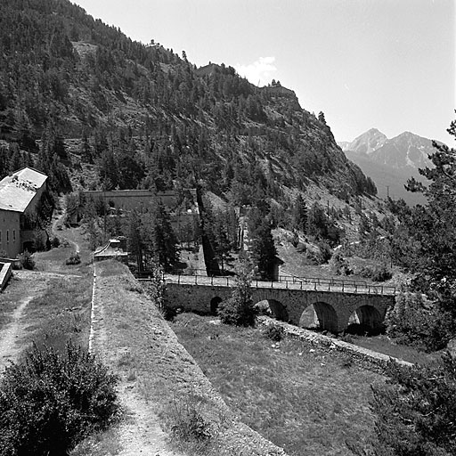 Front ouest. Vue d'enfilade prise dans l'axe du parapet de la courtine. A droite : tenaille/fausse braie, fossé et pont dormant aboutissant à la porte 9. Au fond, flancs étagés du demi-bastion 3 et lacets de la route militaire du fort du Randouillet (au sommet de l'escarpement, murailles du fort). A gauche, bâtiment A.