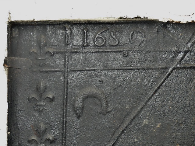 Partie nord. Rez-de-chaussée surélevé, cuisine. Mur sud, cheminée. Plaque foyère : date portée (1650), fleur de lys et dauphin.