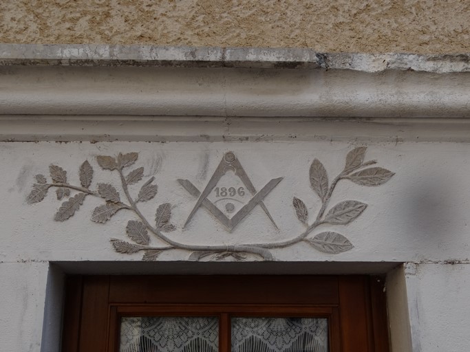 Porte de logis avec linteau droit sculpté d'un compas, d'une équerre et de motifs végétaux accompagnés de la date 1896, et surmonté d'une corniche. Maison située place de l'Eglise au bourg de Ribiers (parcelle 1998 E2 634).