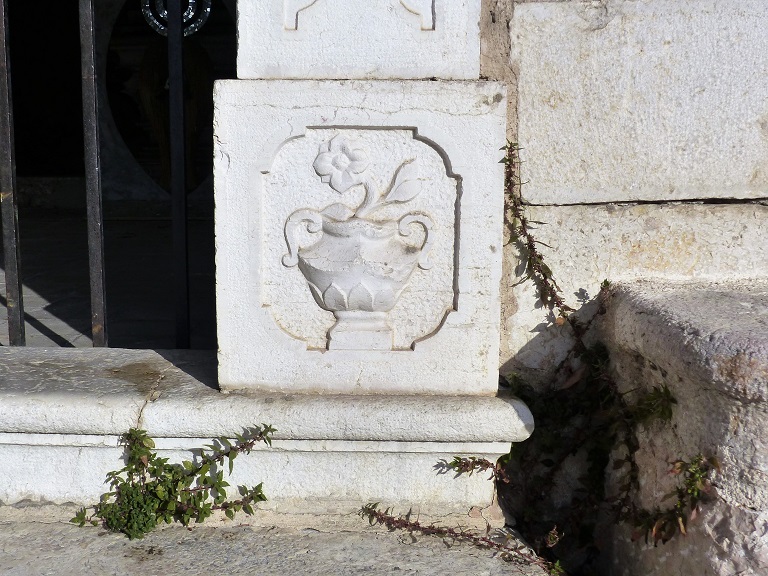 Elévation sud. Détail de la base du piédroit est de l'entrée avec un bas-relief représentant un camélia dans un vase.