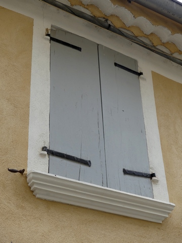 Elévation ouest, second niveau. Fenêtre avec appui saillant en ciment et décor peint de faux encadrement, occultée par des contrevents en planches croisées.