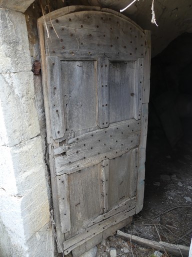 Porte de resserre avec encadrement en arc segmentaire ; menuiserie à panneaux moulurés. Ferme au hameau des Dades (Ribiers).