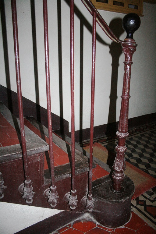 Rez-de-chaussée surélevé. Le départ de l'escalier tournant avec la rampe en fonte de fer.