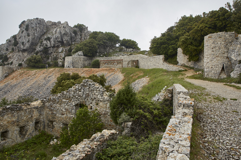 Front de gorge de l'ouvrage, ruines du baraquement crénelé hors enceinte, terrasse et mur d'enceinte à deux saillants flanquants, vus du chemin d'accès.