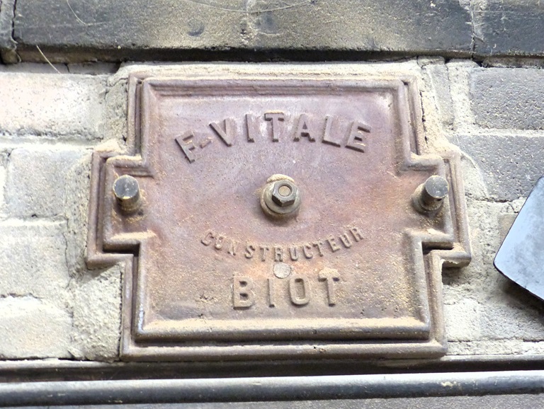 Rez-de-chaussée surélevé, pièce d'enfournement. Mur est, four à pain. Plaque indiquant le nom du fabricant du four F-VITALE / CONSTRUCTEUR / BIOT. 