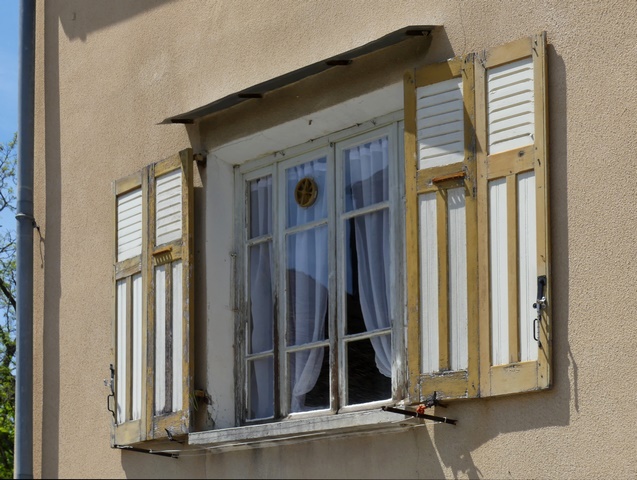 Fenêtre équipée de contrevents à persiennes hautes articulés, ferme agglomérée au bourg.