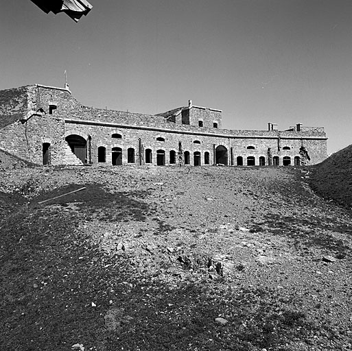 Ensemble du cavalier supérieur du fort vu de l'ouest, depuis la cour centrale. De gauche à droite : abri-magasin H3, escalier d'accès à la batterie et couvrant les latrines D2, façade des casemates A et B (logement de la garnison) surmontée de la batterie, avec traverses H3 et H4.