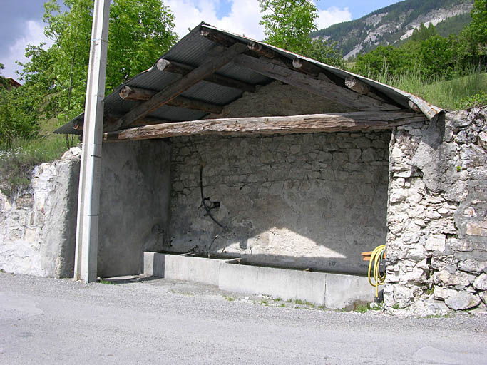 Lambruisse. Fontaine-lavoir. L'édifice, adossé perpendiculairement à la pente contre un mur de soutènement, est fermé sur trois côtés par des murs en moellons calcaires maçonnés.