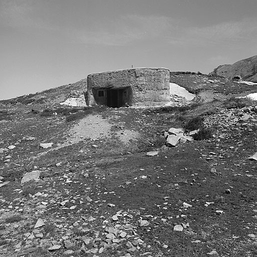 Bloc 1 (entrée). Façade prise de l'ouest. Le béton est brut de décoffrage, le rocaillage non terminé. Sous la visière, à gauche, prise d'air et porte d'entrée. A droite, vu de biais, créneau FM de la caponnière.