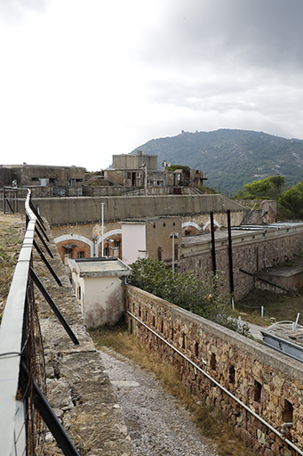 Revêtement d'enceinte de la batterie, détail du front de gorge de l'aile gauche, mur-parapet crénelé bordant la rampe carossable; au fond, casernement sous l'aile droite