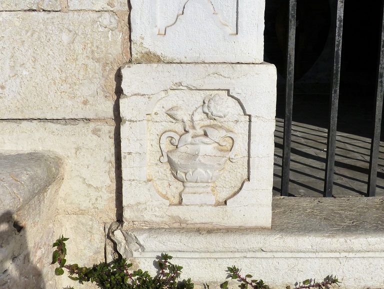 Elévation sud. Détail de la base du piédroit ouest de l'entrée avec un bas-relief représentant une rose dans un vase.