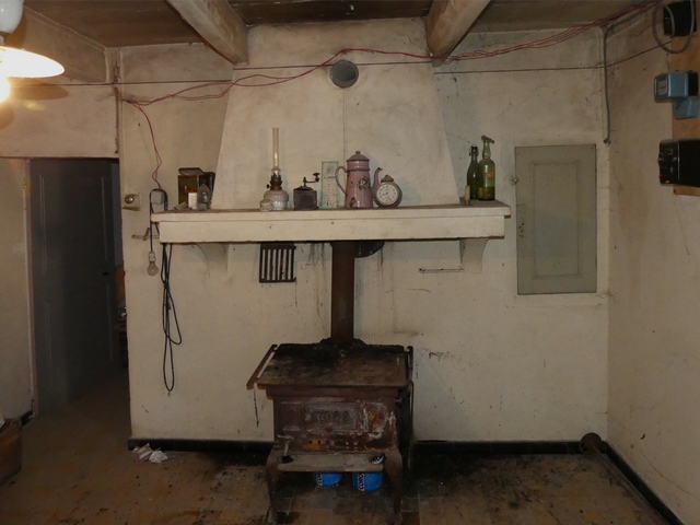 Rez-de-chaussée surélevé, cuisine. Mur sud : porte de la chambre, cheminée et petit placard-niche.