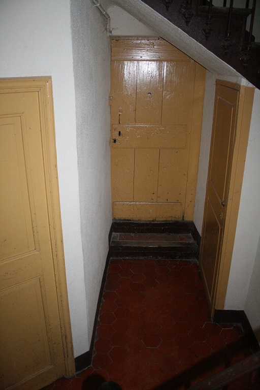 Rez-de-chaussée surélevée. Le couloir de distribution avec le coude. A gauche, la porte menant à l'ancienne cuisine.  A droite, la porte ouvrant sur l'escalier qui mène au cellier. Au fond, la porte menant à une pièce d'habitation (ancienne parcelle 271).