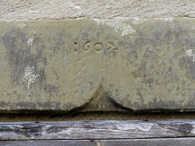 Elévation nord, premier niveau. Porte du logis ouest, linteau chanfreiné à accolade retaillé en feuillure portant une date gravée (1602).