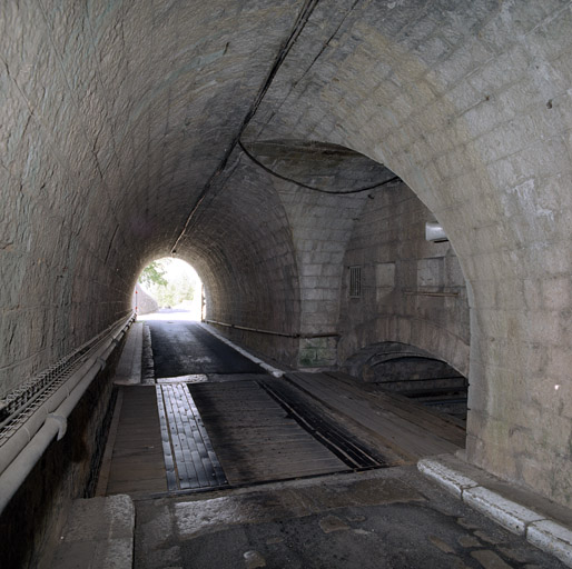 Intérieur du tunnel de sortie du fort vers le plateau (reste de la forteresse) au premier plan, fosse à pont mobile et corps de garde crénelé.