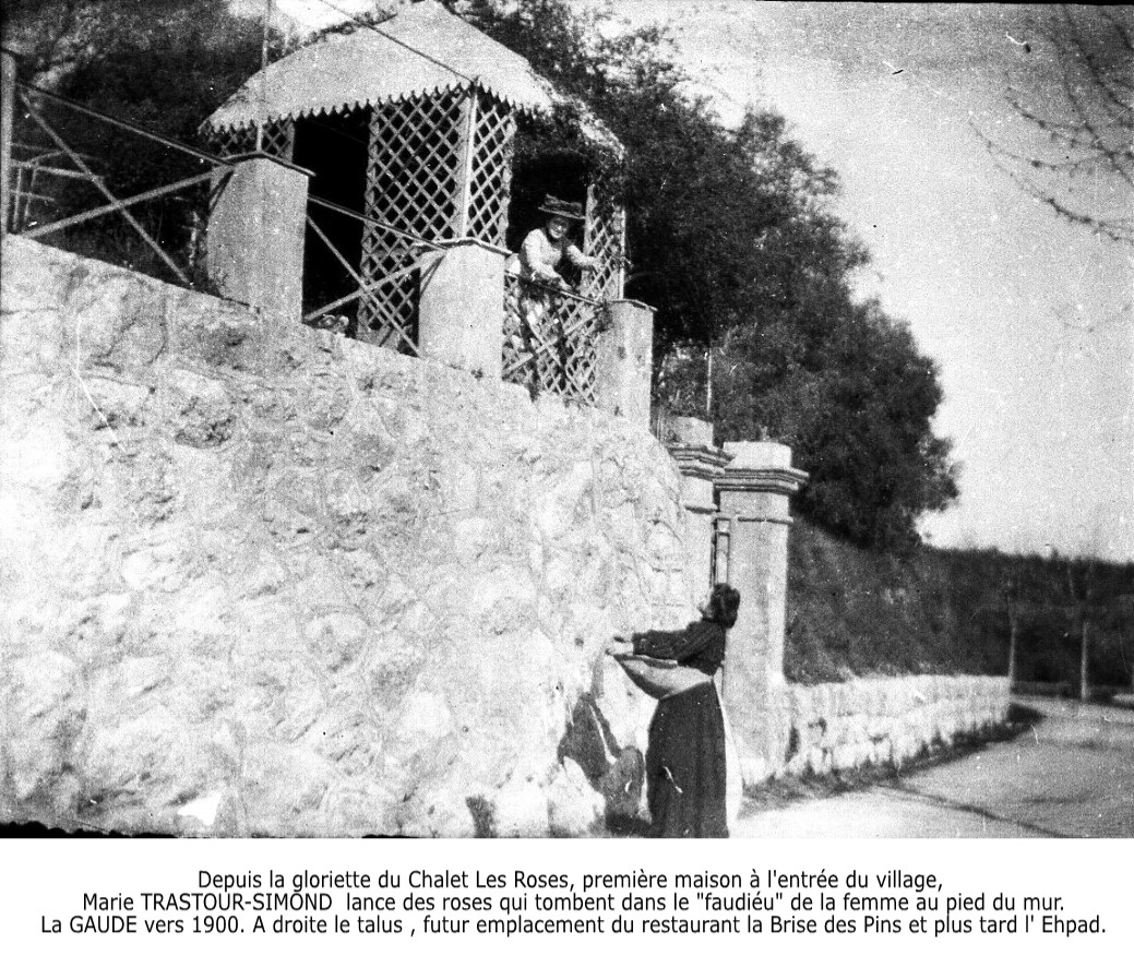 [Depuis la gloriette du Chalet Les Roses, première maison à l’entrée du village, Marie TRASTOUR-SIMOND lance des roses qui tombent dans le « faudiéu » de la femme au pied du mur. La Gaude vers 1900. A droite le talus, futur emplacement du restaurant La brise des Pins et plus tard l'Ehpad.] 