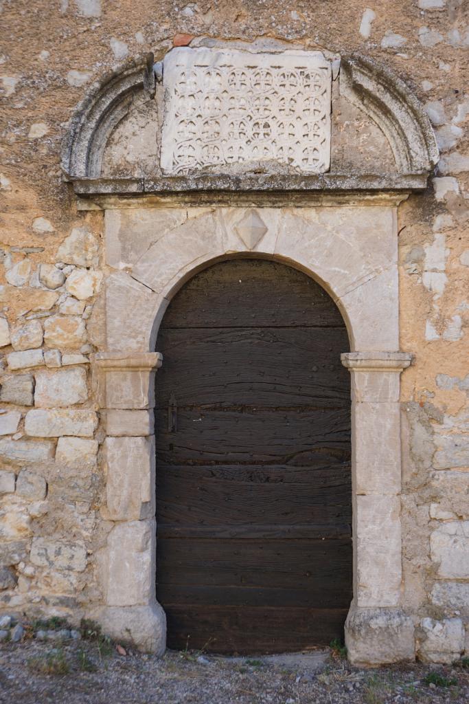 Détail de la façade principale : porte latérale avec plaque de chancel en remploi.