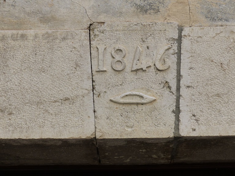 Maison (2023 B 574a). Date portée sur la clé de la plate-bande : 1846. Une navette est représentée et indique la profession de tisserand du propriétaire. 