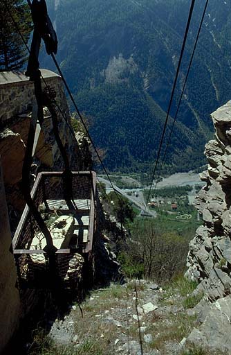 Téléphérique. Vue plongeante prise de la recette supérieure dans l'axe du câble. En bas, le bâtiment de la recette inférieure. A gauche, benne et, derrière, mur d'enceinte du front sud.