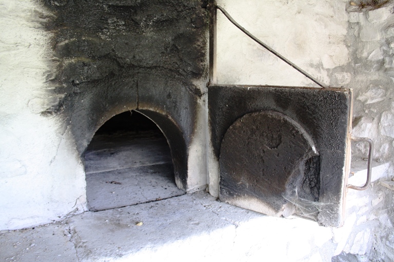 Colmars. Chaumie Haut. Bouche du four appareillée en arc en plein-cintre et porte en grès fixée sur une potence métallique.