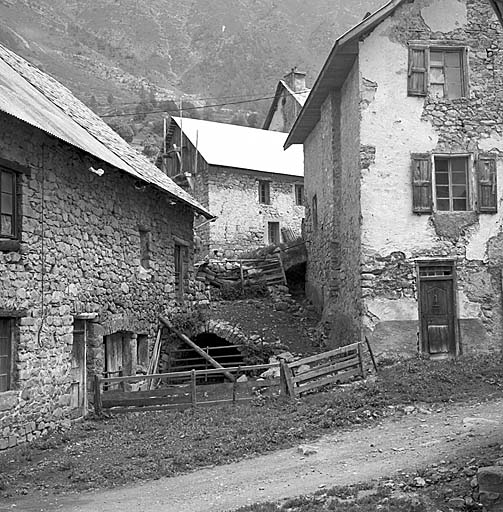 ferme n°2 : le mur nord, vue partielle. Noter l'arc de pierres qui supporte le montage. ferme n°5 : Façade en mur gouttereau. A noter les plates-bandes qui surmontent les ouvertures, les deux voûtes en berceau des montages, la saillie que fait la cheminée sur le mur de gauche et l'enclos pour le bétail devant la porte de l'écurie.