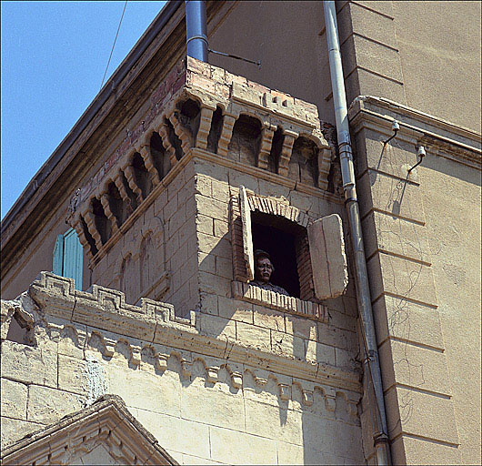 Détail de la façade de la chapelle. Décor de rocaille en trompe l'oeil : tourelle à mâchicoulis, faux appareil, créneaux, personnage apparaissant à une fenêtre.