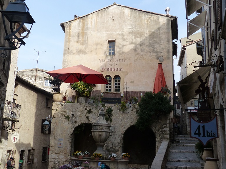 Maison (2022 AY 190). Façade avec décor peint : inscription effacée "Chez George restaurant", recouverte par "Hostellerie/de la/Fontaine". Au sommet, subsistent les traces d'un cadran solaire. 