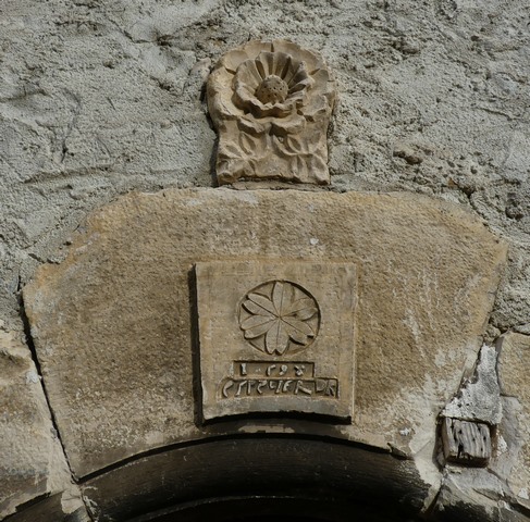 Bâtiment du logis. Elévation ouest, premier niveau. Porte du logis : cartouche sculpté et date en réserve (1598) accompagnée de l'inscription « ESP. R[EN]IER », surmontée d'une sculpture de rose en bas relief.