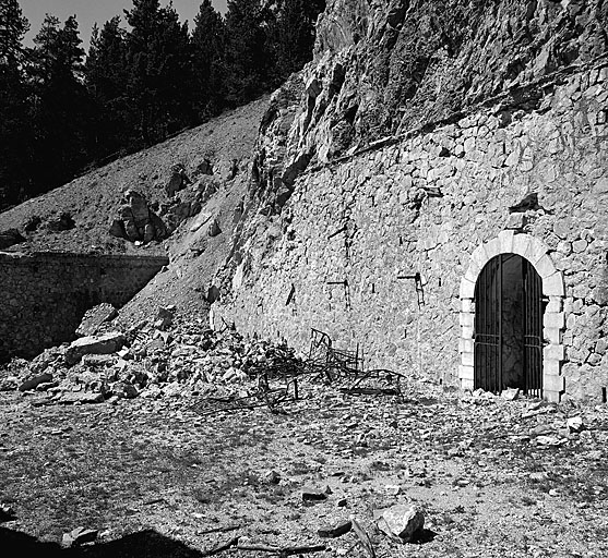 Magasin à poudre : vue intérieure de la cour et façade de l'ouvrage. A droite, entrée nord des casemates-cavernes. A gauche, débris du local 4 et éboulement masquant l'entrée de la galerie sud.