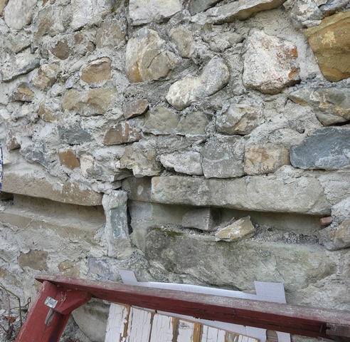 Cour. Mur sud, pierres rainurées du trou de barre du portail, remployées.